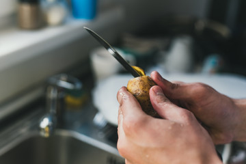 man cleans potatoes with a knife at the sink at home. peel small potatoes. cleaning in the sink.