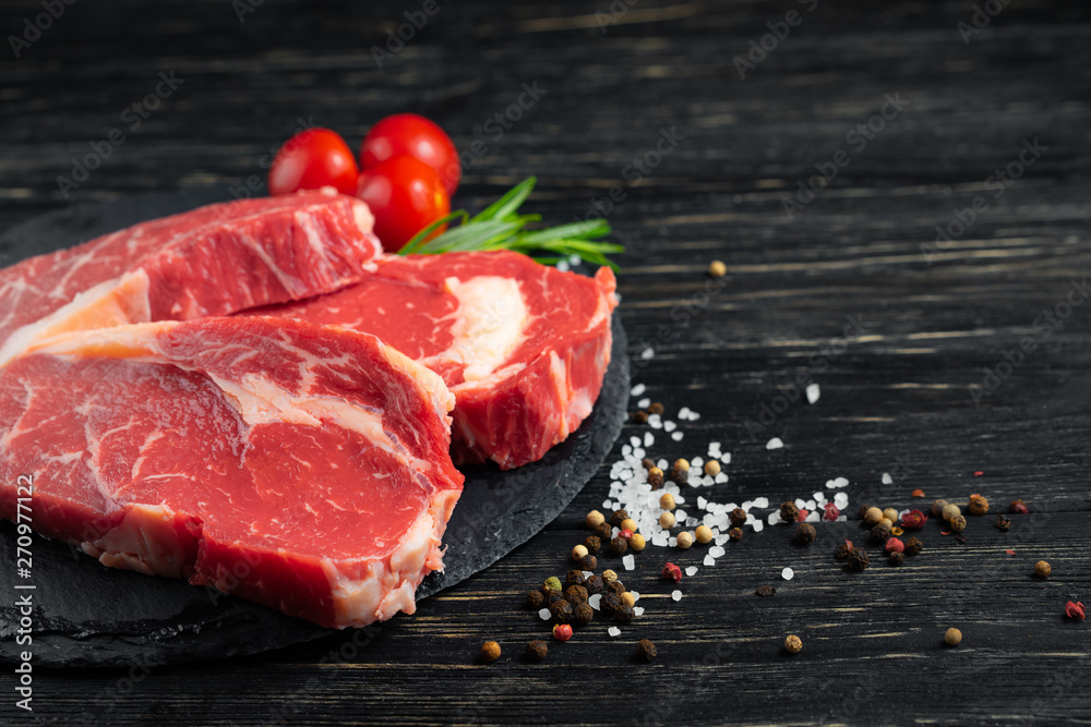 Wall mural Three pieces of juicy raw beef on a stone cutting board on a black wooden table background.