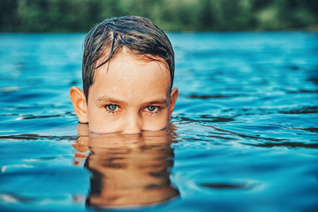 portrait of a child in the water. boy with beautiful eyes swimming in a pond