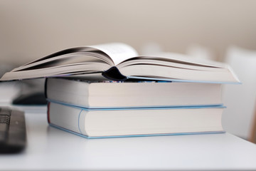 Open book on a stack of books on a table.