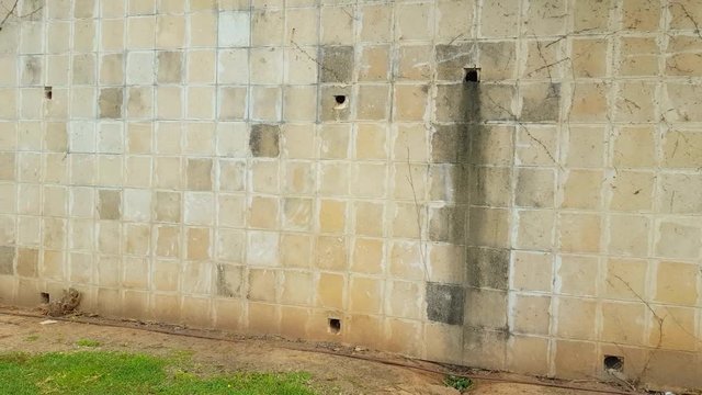 Camera moves along tiled exterior wall with big mildew stain. Quiet residential area with 2 story houses.