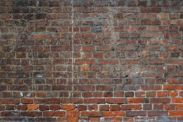 Urban wall from a red brick with a regular laying with scratched surface and grange stains