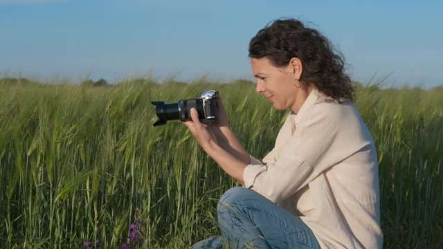 A female photographer takes pictures in nature. Pretty woman with a camera in the field.