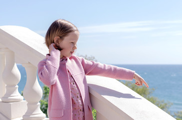 Fototapeta na wymiar Little cute girl (7 years old) is standing against the sea in a pink outfit.