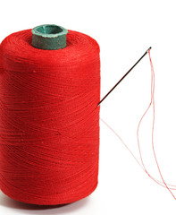 Sewing spool and a needle and cotton of red color on white background, isolated, closeup