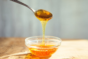 Honey dripping from spoon into the glass bowl