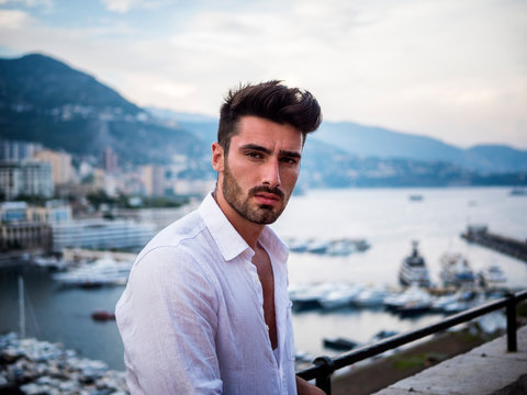 Attractive fit athletic young man soaking in the sun on seaside boardwalk or seafront, wearing white shirt in Montecarlo, Monaco on the French Riviera