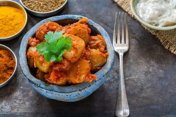 Bombay aloo - Indian spiced potatoes with tomato sauce and minted yogurt, garnished with fresh coriander leaves.