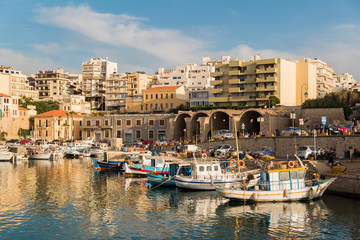view of heraklion old port on a clear day. calm blue water boats floating and coastal road and buildings as background