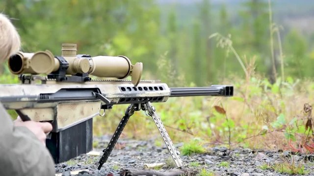 Sniper rifle shoots in slow motion on far away targer. Forest, summer.