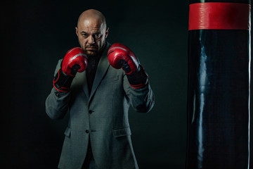 Businessman and sportsman in suit, man boxer in gloves with boxing punching bag. Trainings and