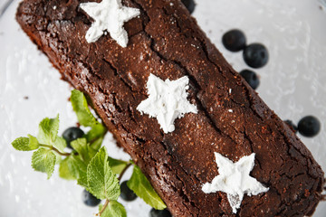 Closeup of a brownie chocolate cake with fresh blueberries, white powdered sugar stars and mint leaves. Homemade cake decorated with fruit. Festive concept. Selective soft focus
