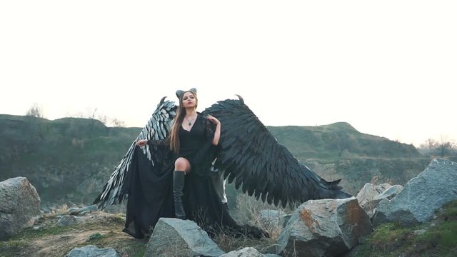 mysterious lady in black light lace dress with long train, girl with open leg in leather boots, dark horned angel from heaven, messenger of death with large wings on edge