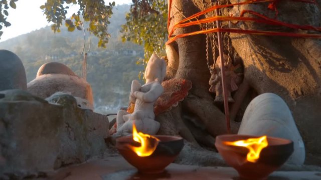 Stone figure of the Indian God on the banks of the sacred Ganges River in the light of sunset, in the city of Rishikesh, India, candles are burning and incense is smoked nearby. Slow mo, slo mo, slow 