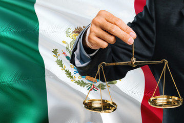 Mexican Judge is holding golden scales of justice with Mexico waving flag background. Equality theme and legal concept.