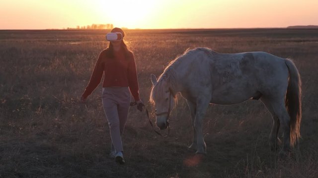 Pretty girl in glasses virtual reality leads white horse across the dried field
