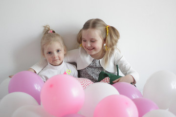 Fototapeta na wymiar two girls play in bed with white and pink balloons and a strawberry pillow