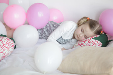 Fototapeta na wymiar a girl plays in bed with white and pink balloons and a strawberry pillow