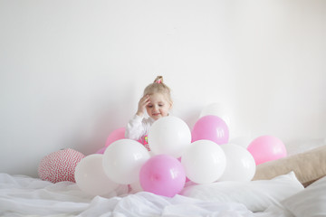 a girl plays in bed with white and pink balloons and a strawberry pillow