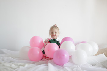 a girl plays in bed with white and pink balloons and a strawberry pillow