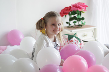 Obraz na płótnie Canvas a girl plays in bed with white and pink balloons and a strawberry pillow