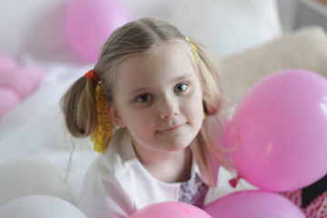 a girl plays in bed with white and pink balloons and a strawberry pillow