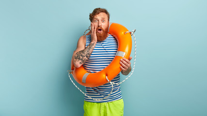 Impressed redhaired man has nervous facial expression, afraids of swimming in ocean for first time,...