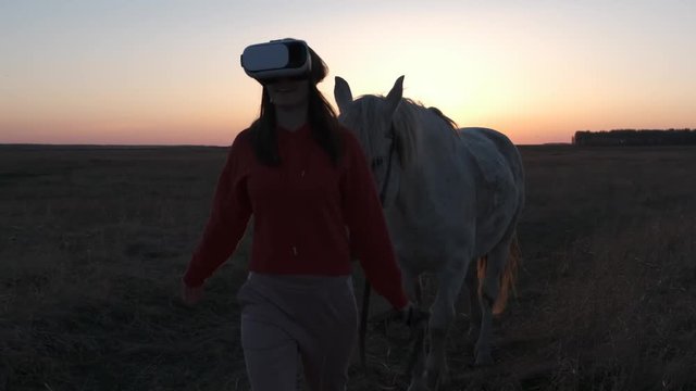 Girl and glasses of virtual reality leads a white horse along an endless field