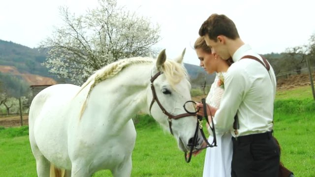Bride with groom holding white horse to side of them and wedding teepee making background in nature.