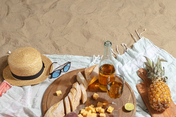 Picnic on a sandy beach with white wine, snacks and fruit on a blue plaid.