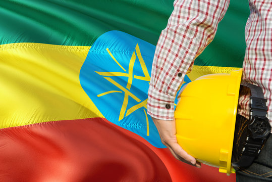 Ethiopian Engineer is holding yellow safety helmet with waving Ethiopia flag background. Construction and building concept.