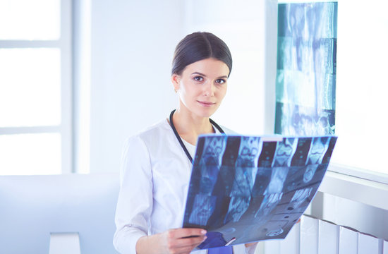 Young smiling female doctor with stethoscope looking at X-ray at doctor's office