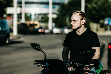 brutal male motorcyclist with glasses sitting on a motorcycle. Motobike driver in the city.