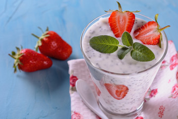 Healthy and tasty yogurt detox smoothie with chia seeds and pieces of ripe strawberries in a glass on a napkin and blue background next to pair of fresh strawberries