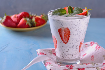 Healthy and tasty yogurt detox smoothie with chia seeds and pieces of ripe strawberries in a glass on a napkin and blue background next to a few fresh strawberries