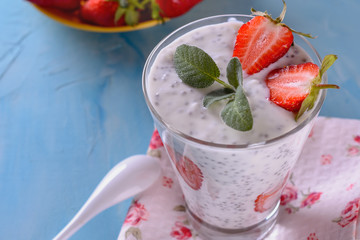 Healthy and tasty yogurt detox smoothie with chia seeds and pieces of ripe strawberries in a glass on a napkin and blue background next to a few fresh strawberries
