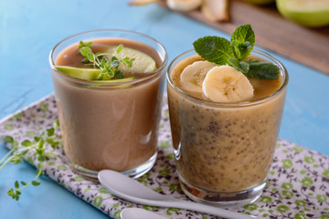 Healthy and tasty yogurt detox smoothies with chia seeds, greenery, bananas, apples and other green ingredients and pieces of ripe bananas in a glasses on a napkin and blue background, closeup