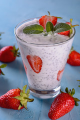 Healthy and tasty yogurt detox smoothie with chia seeds and pieces of ripe strawberries in a glass on a blue background next to some few strawberries, vertical orientation