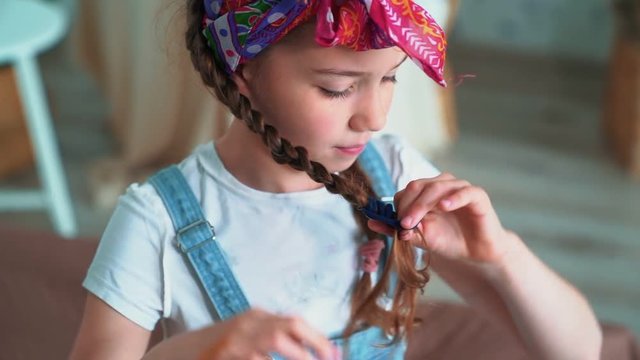 Portrait of cute girl ties braid with scrunchy and looks at camera, slow motion