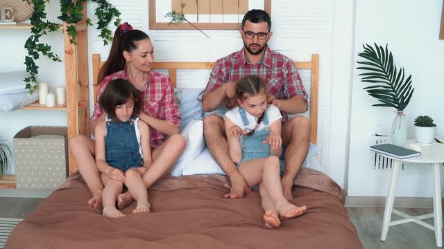 Parents do massage for two daughters, sit on bed, laugh and have a good time