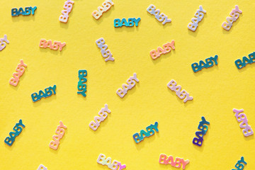 Pastel colored confetti with word baby scattered on yellow background. Gender neutral modern trendy baby shower template for invitations, greeting cards, banners, albums. Flat lay, paper cut.