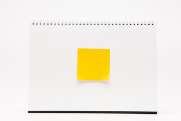 Yellow sticker with A white paper calendar stands on the table in photo