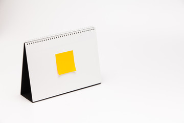 Yellow sticker with A white paper calendar stands on the table in photo