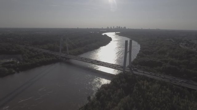 Flying over the river hung through a busy road. Warsaw downtown on the background at sunset. Panoramic aerial view of Warsaw Siekierkowski Bridge with the river in the background. 4K drone in RAW.