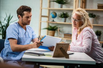 General practitioner and mature woman going through medical documents together.