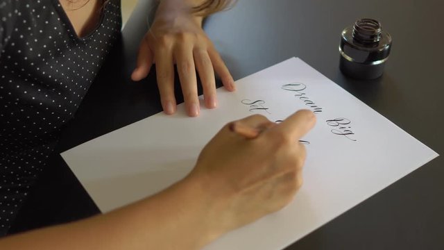 Close up shot of a young woman calligraphy writing on a paper using lettering technique. She writtes Dream big Set goals Take action