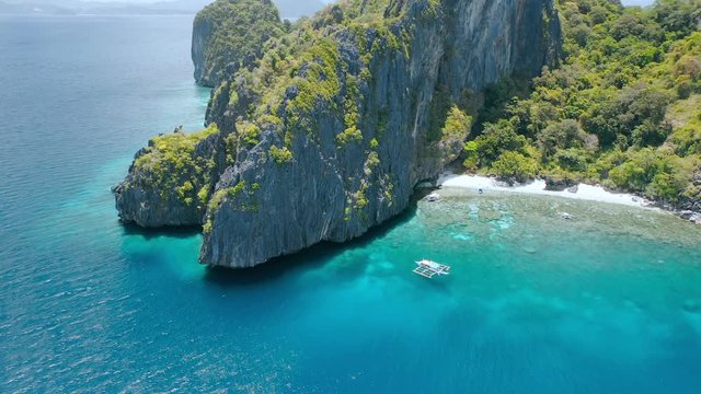 Aerial circle fly above coral reef and banca boats at the beach of limestone rocky Entalula Island, Bacuit Bay, El-Nido. Palawan Island, Philippines