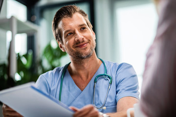 Smiling male doctor talking to his patient while going through medical reports at his office.