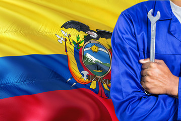 Ecuadorean Mechanic in blue uniform is holding wrench against waving Ecuador flag background. Crossed arms technician.