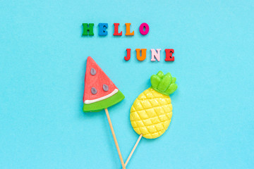 Hello June colorful text, pineapple and watermelon lollipops on stick on blue paper background. Concept vacation or holidays Creative Top view Template Greeting card, postcard